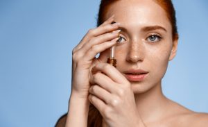 face of woman with freckles applying serum